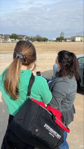 Two individuals  standing in a parking lot, holding donation bags, surveying an individual who is not pictured