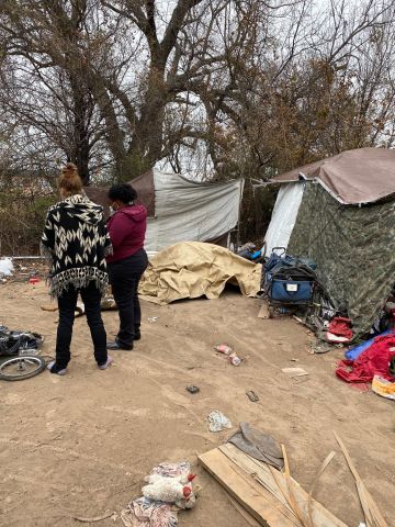 Two individuals in an encampment, surveying an individual not pictured